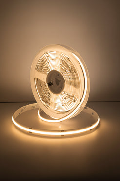 A coiled white LED light strip product displayed on a reflective surface against a cool blue-gray gradient studio background.